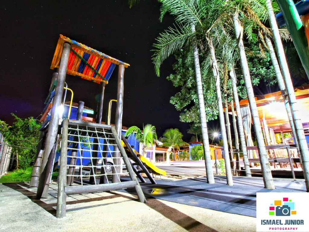 Playground infantil da pousada iluminado à noite sob palmeiras e céu estrelado